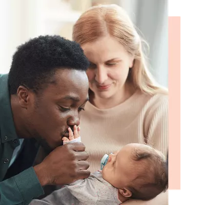 Woman holding her baby while father kisses the childs hand