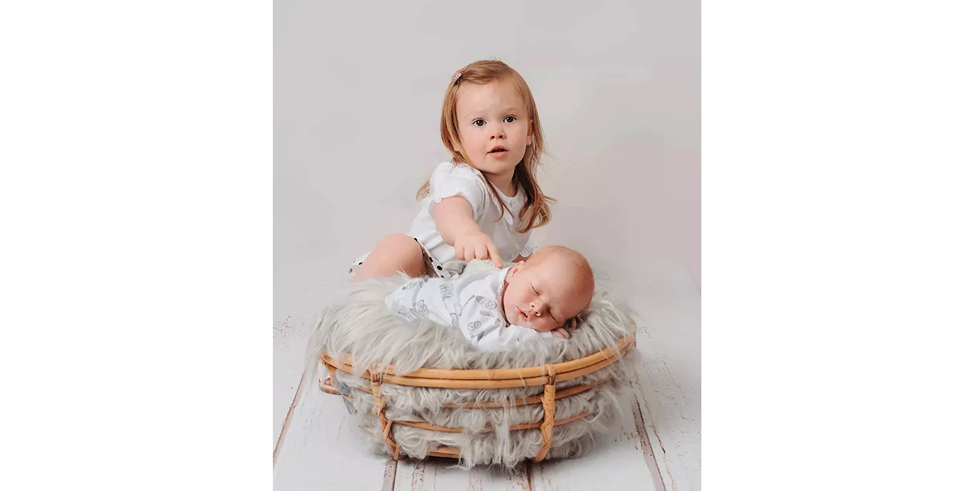 Photo of a toddler holding her hand on her baby sibling