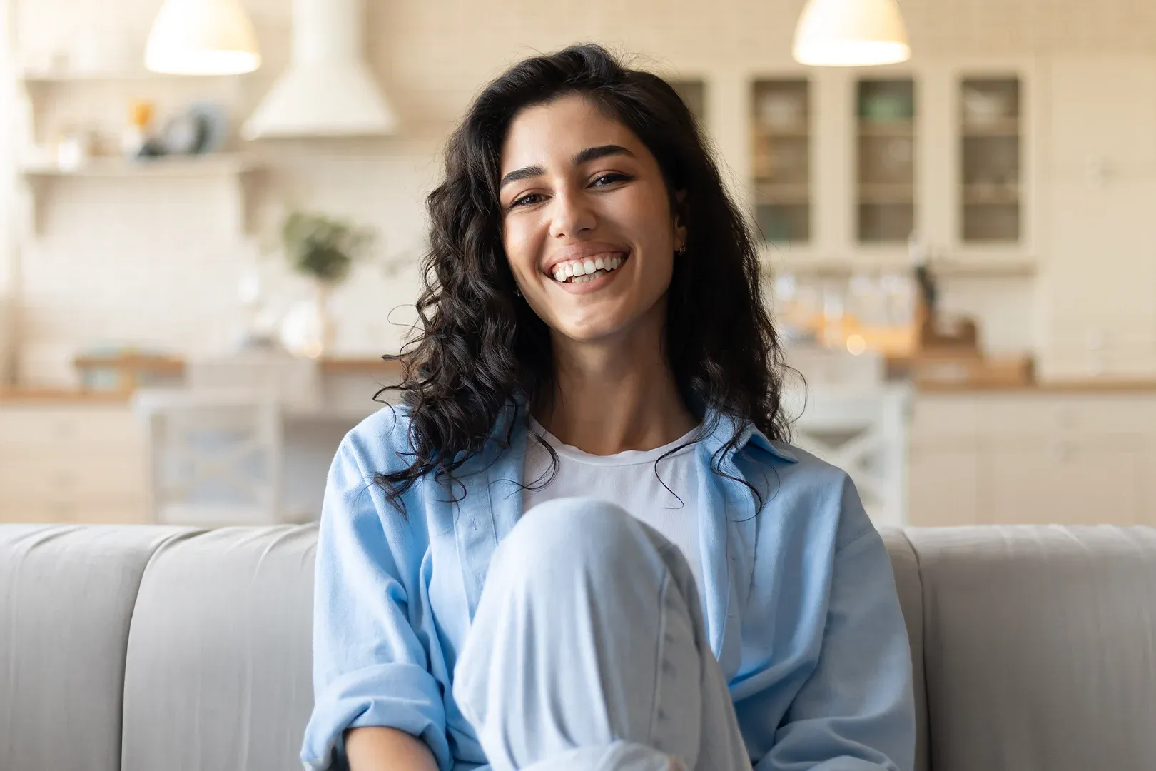 confident smiling women sits on couch of her modern apartment smiling at the camera