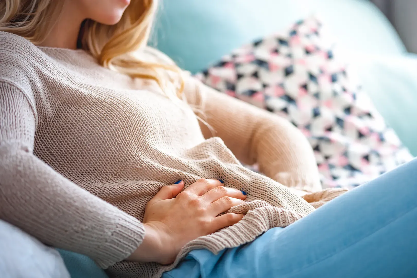 a woman sits on a sofa holding her stomach while experiencing cramps and light bleeding