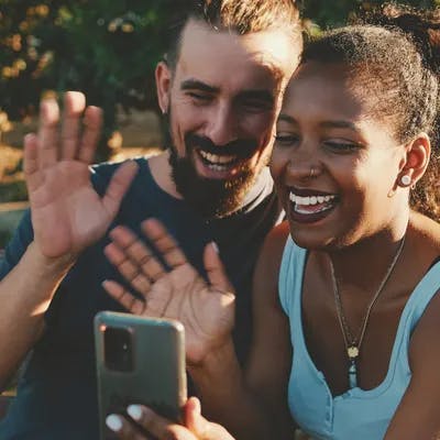 A young couple smiling and waving at someone through their phone