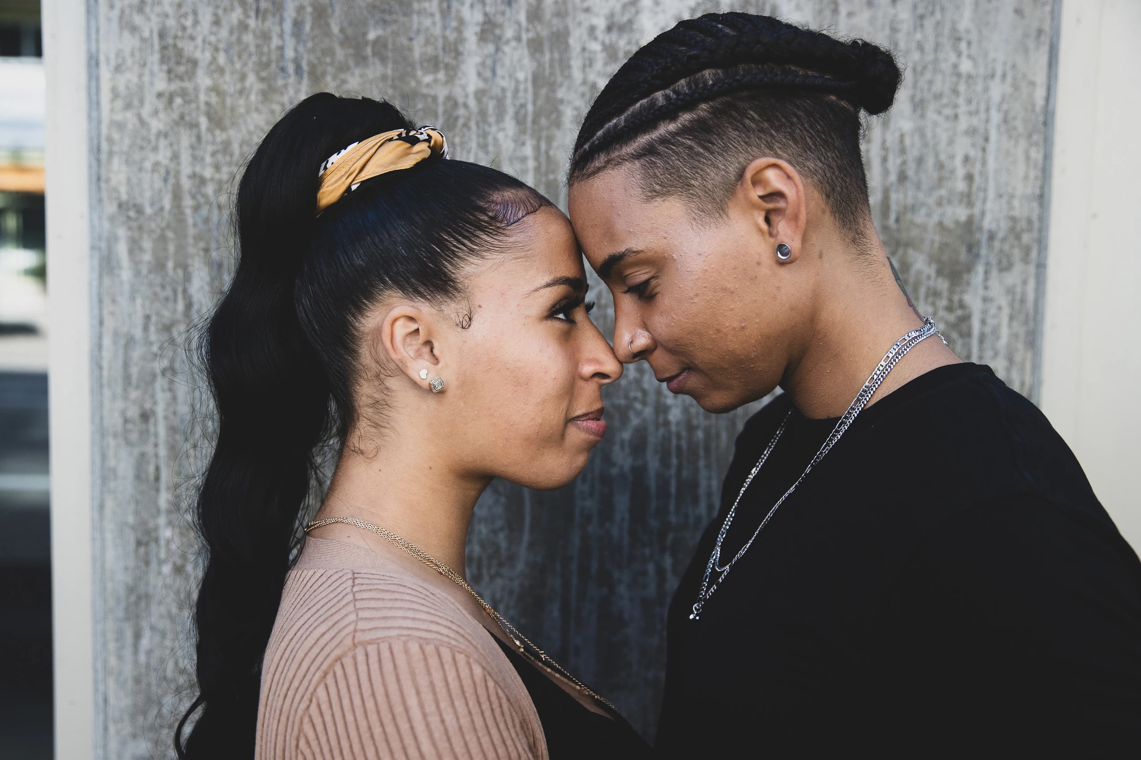 A young female couple stood facing each other, resting their foreheads together