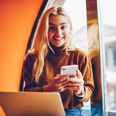 Young girl sat with a laptop using her phone